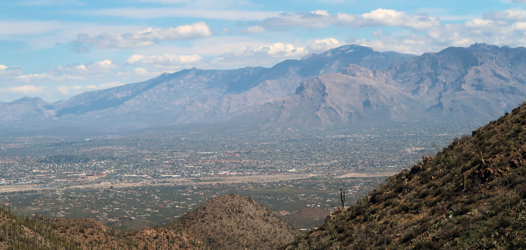 Tucson sprawls beyond the ridgeline below Wasson Peak. Beyond the city rise much taller mountains, including Mt Lemmon.